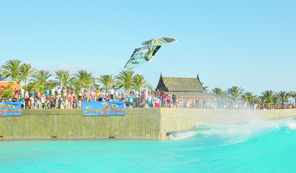 Surfer jumping in wave pool in Siam Park, Tenerife, under clear skies.