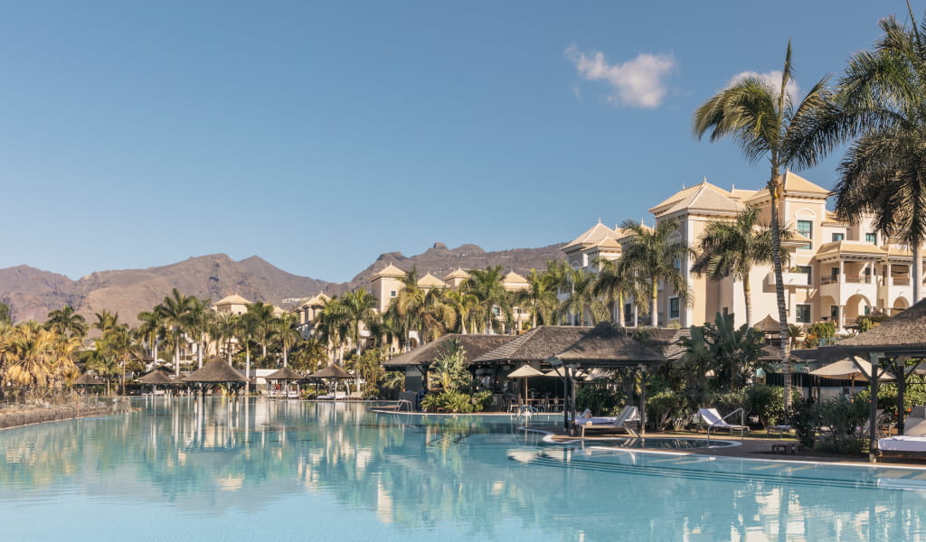 Swimming pool and palm trees in front of a hotel in Tenerife, with mountain in the background.