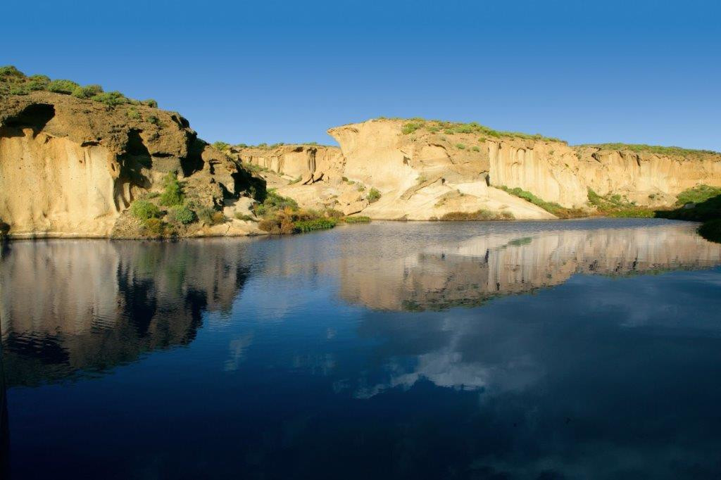 Rock formations reflected in water under a clear sky in Tenerife.