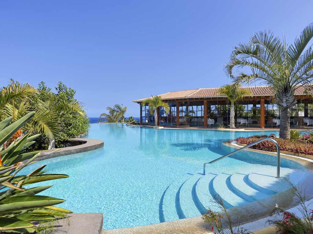 Swimming pool surrounded by palm trees and restaurant in Tenerife.
