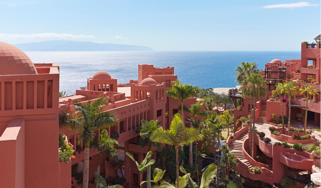 Terracotta-coloured buildings with sea views in Tenerife, surrounded by palm trees.
