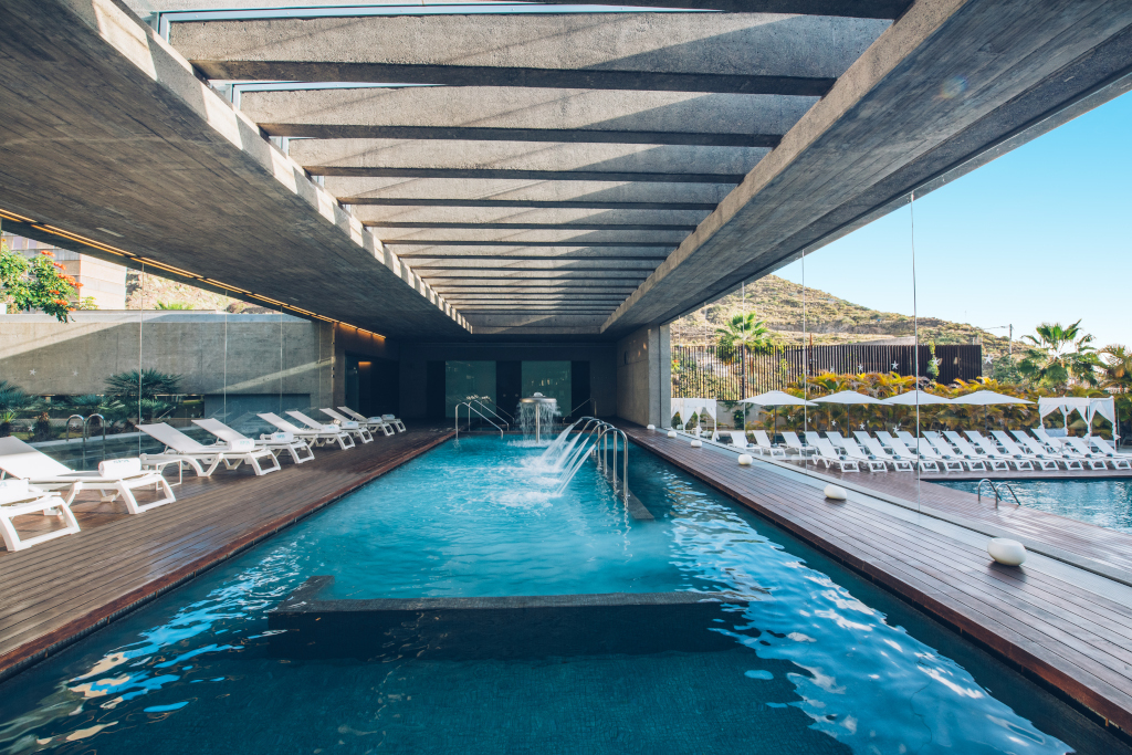 Indoor swimming pool with sun loungers arranged all around, mountain views in Tenerife.