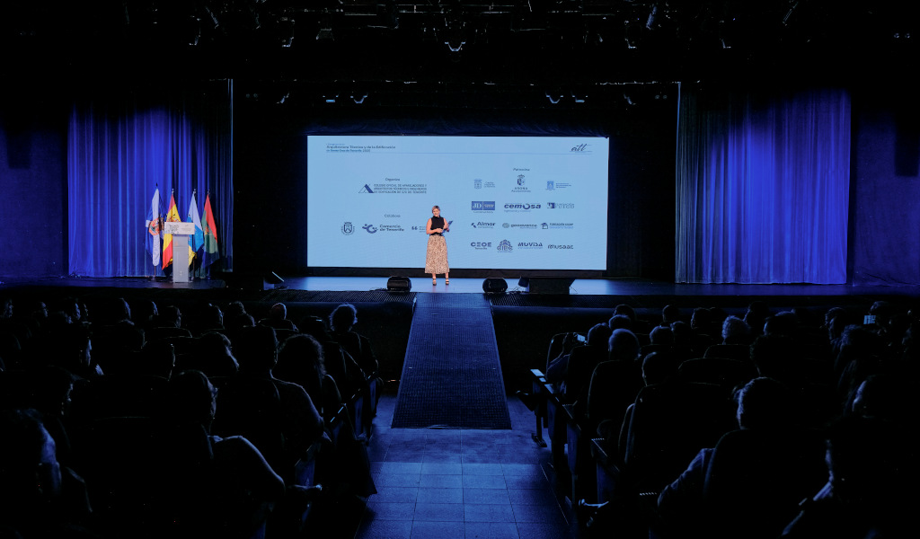 Person on stage during conference instead of Tenerife, with logo projection.