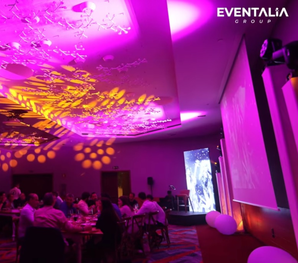 Crowd at a party with lights and a screen showing Camino de Oz in Santa Cruz de Tenerife.