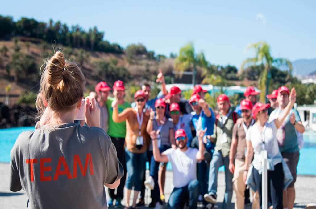 Group of people wearing red caps posing by a swimming pool in Tenerife.