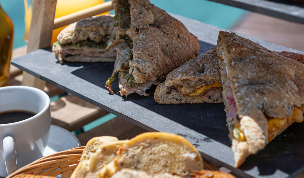 Ham and cheese sandwiches on a board, with a cup of coffee, on a terrace in Tenerife.