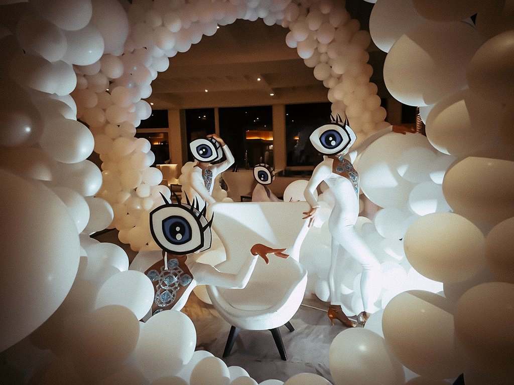 Performers in eye costumes surrounded by white balloons in Tenerife venue.
