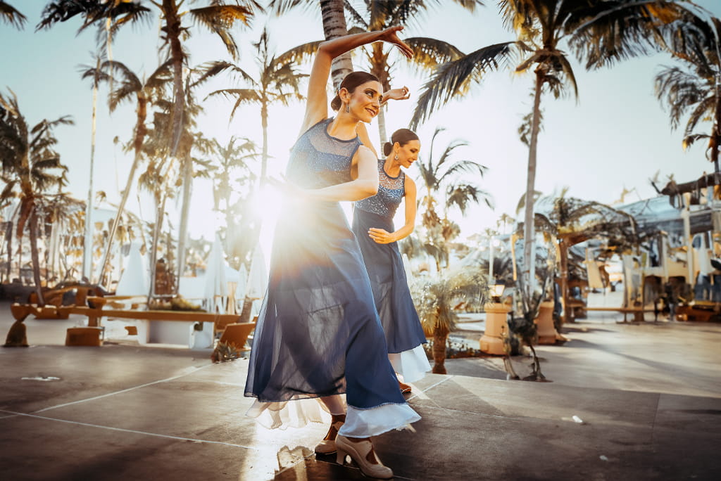 Dancers in blue dresses under palm trees in Tenerife with the sun shining.