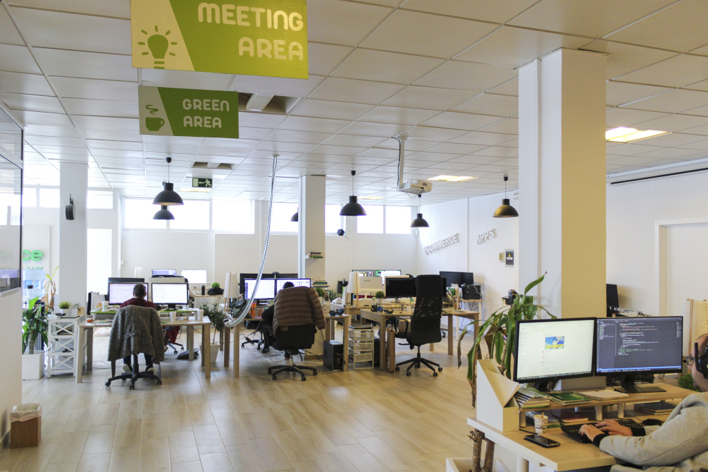 Open-space office in Tenerife with multiple desks and signs for Meeting Area and Green Area.