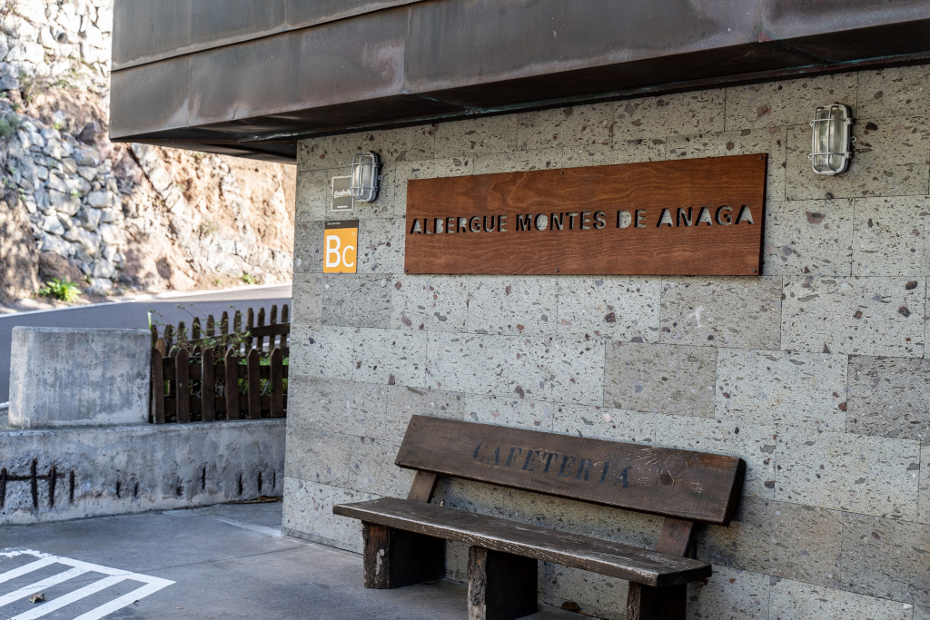 Entrance sign of Albergue Montes de Anaga with a bench labeled 'Cafetería'.
