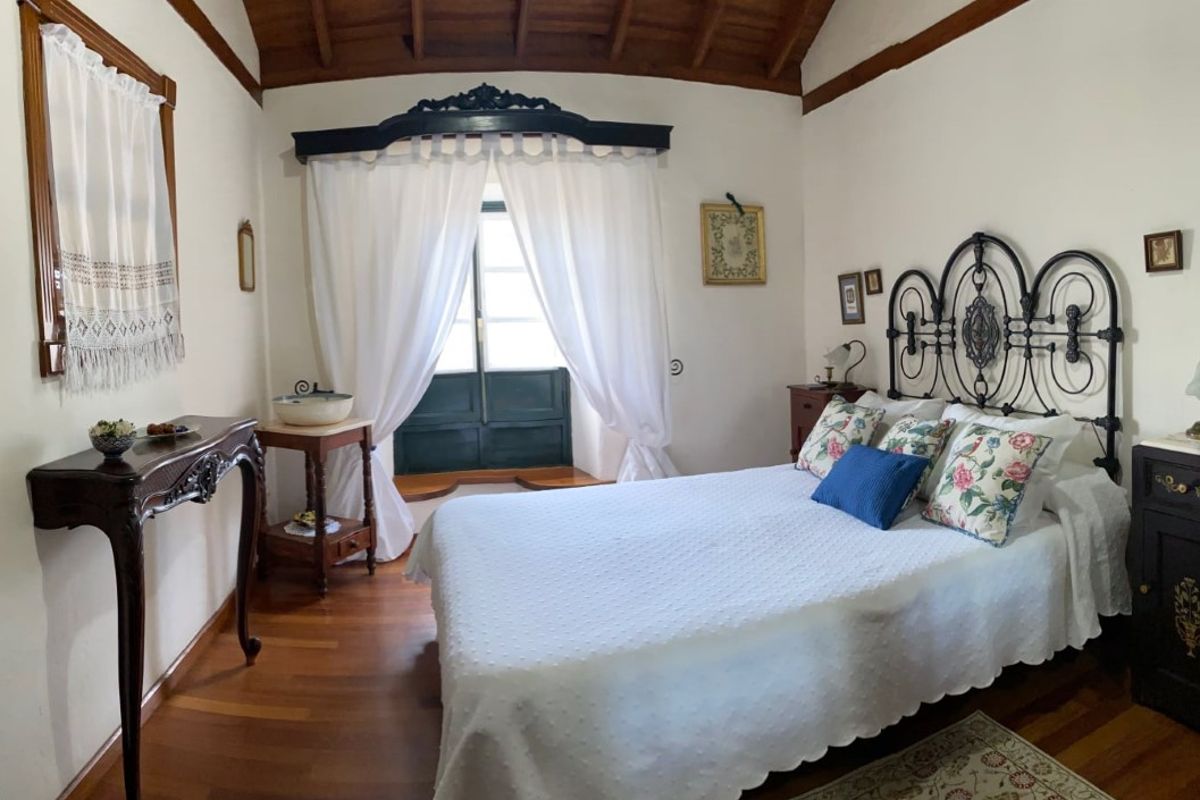 Bedroom with white bedspread, floral pillows, and dark wood furniture in La Orotava, Tenerife.