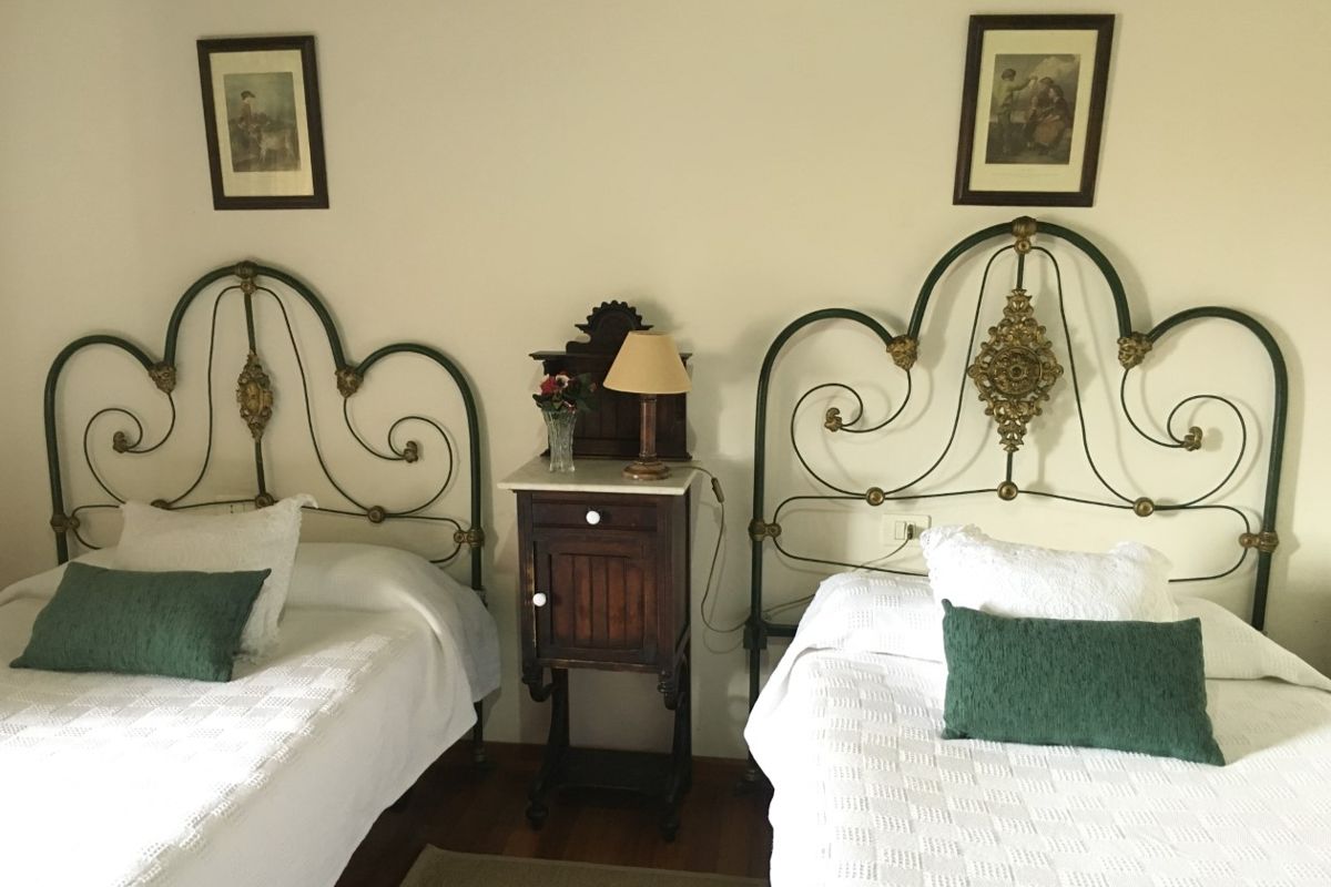 Two single beds with ornate metal headboards and a nightstand with a lamp in a room in Tenerife.