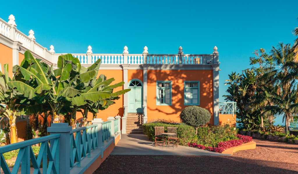 Orange colonial house with banana trees and flowers in Tenerife garden.