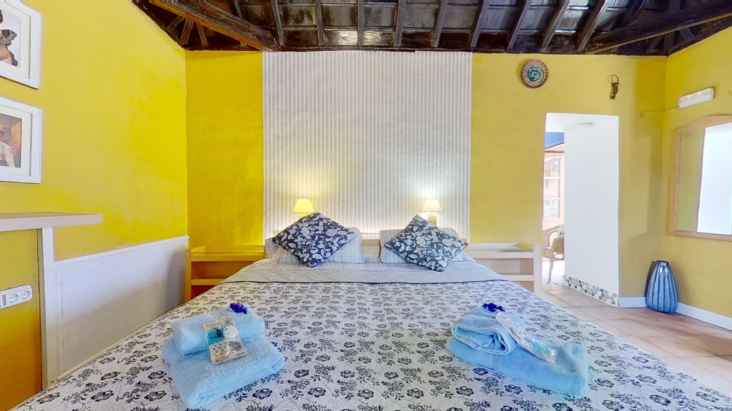 Cozy bedroom with yellow walls, patterned bedspread, pillows, and towels; Tenerife.