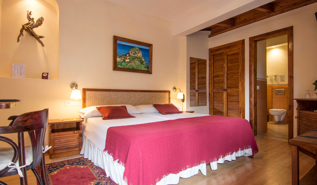 Double bed with red bedding in a hotel room in Tenerife, featuring a painting and bathroom door.