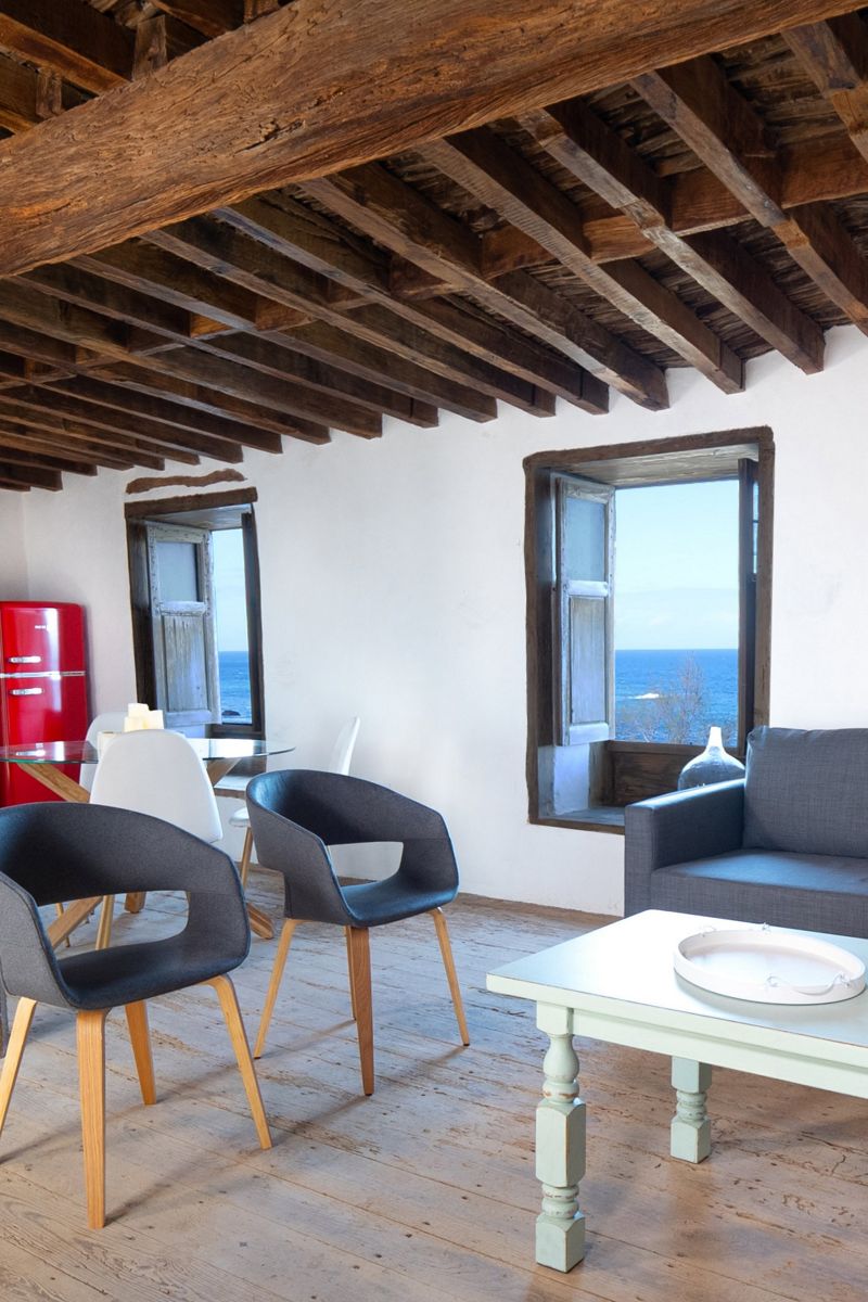 Living room with chairs, table, and ocean view through window in Tenerife house.