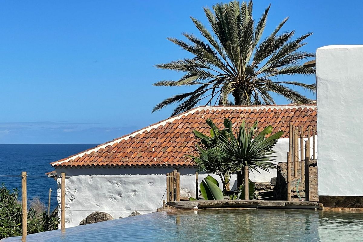 Terracotta roof house by the sea in Tenerife, with palm tree and pool in foreground.