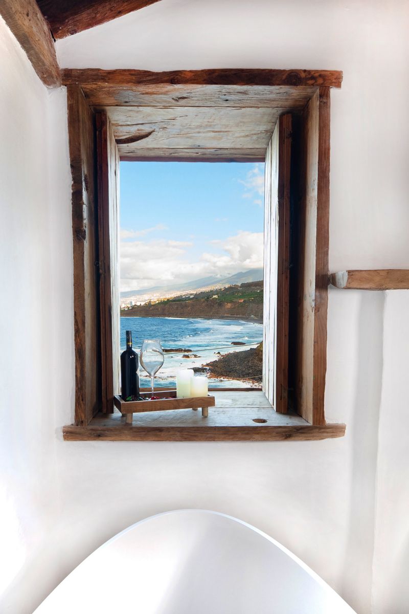 View of Tenerife coast through a rustic window with wine bottle and glass.