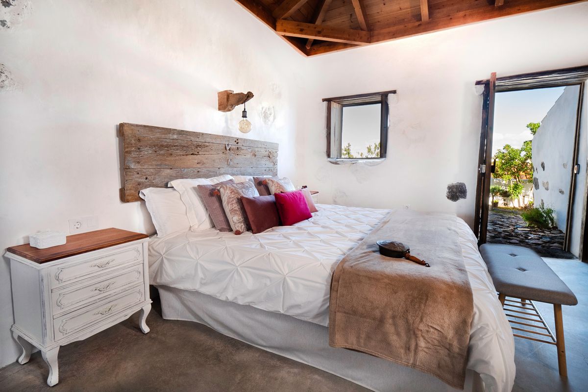 Bedroom with rustic wooden headboard and open door in Tenerife.