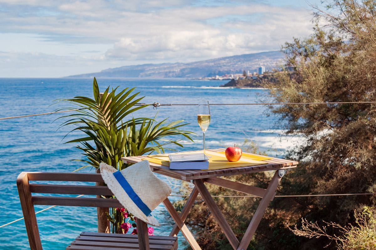 A wooden table with a glass of wine, book, and apple by the sea in Puerto de la Cruz, Tenerife.