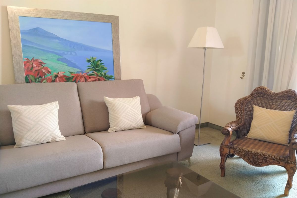 Sofa and wicker chair in a living room with a painting of Tenerife landscape.