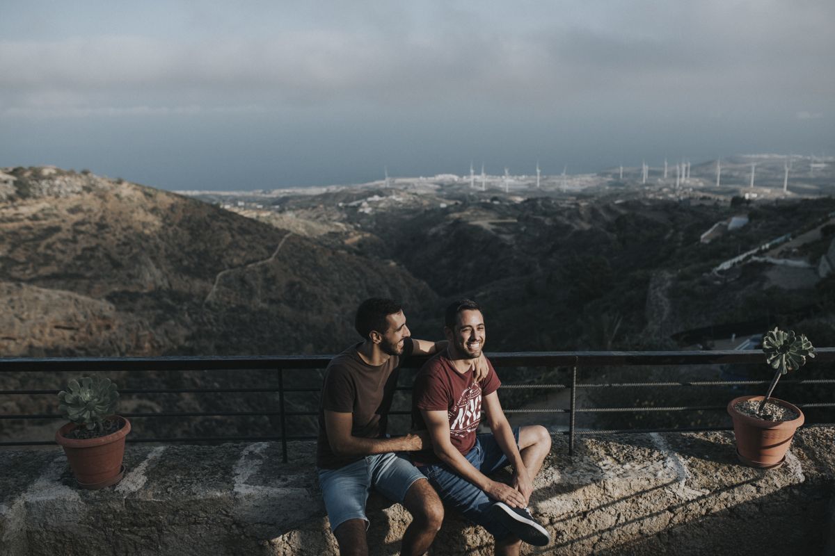 Two people sitting on a stone wall with Tenerife landscape in the background.