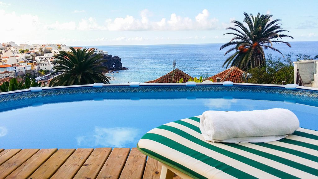 Outdoor pool overlooking the sea and town in Tenerife, with a towel on a striped lounge chair.