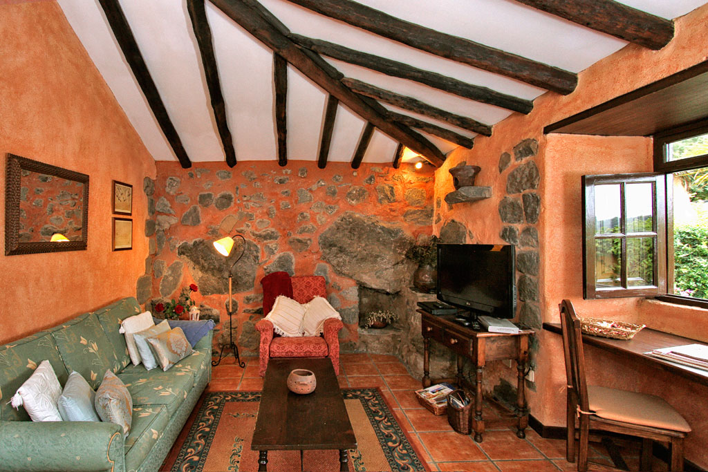 Cozy living room in Tenerife with stone walls, wooden beams, and rustic furniture.