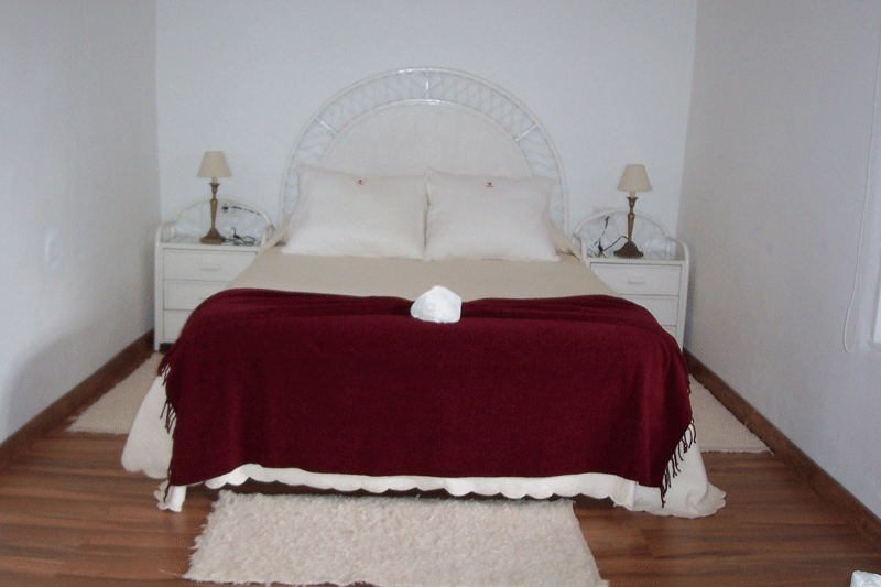 Double bed with red blanket, pillows, two nightstands, and lamps in Tenerife room.