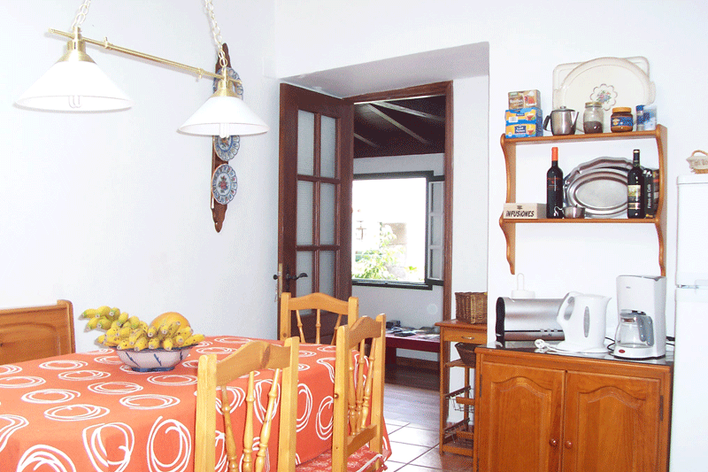 Dining room in Tenerife with table, chairs, and kitchen shelves displaying items.