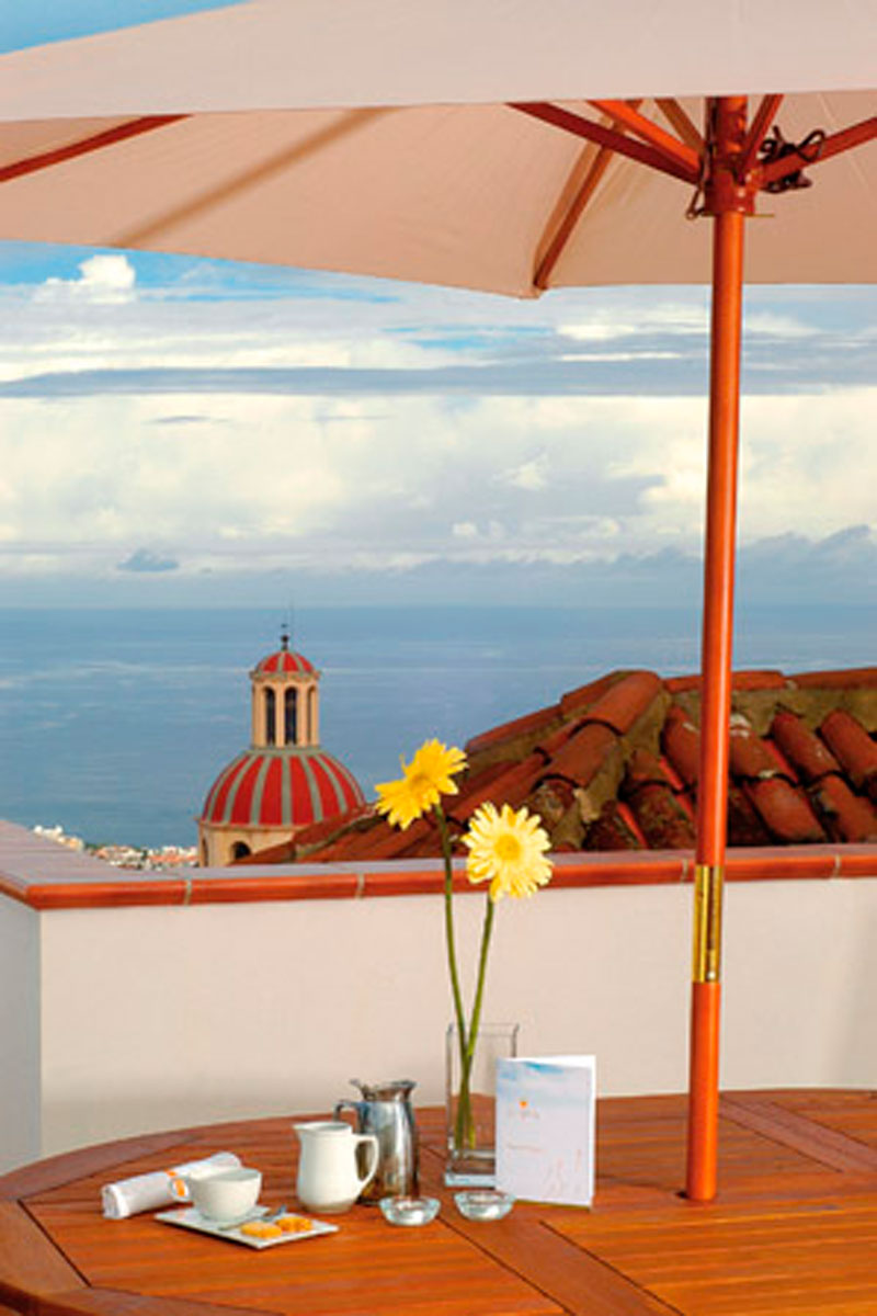 Terrace view of ocean and La Orotava with coffee set and flowers on table.