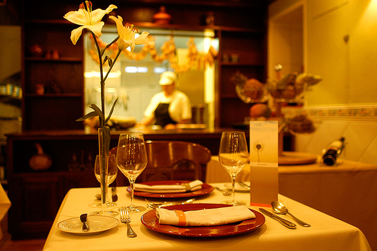 Restaurant table with lilies, cutlery, wine glasses, and chef cooking in Tenerife kitchen.