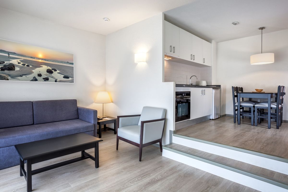 Living room in Tenerife with sofa, armchair, and kitchen in the background.