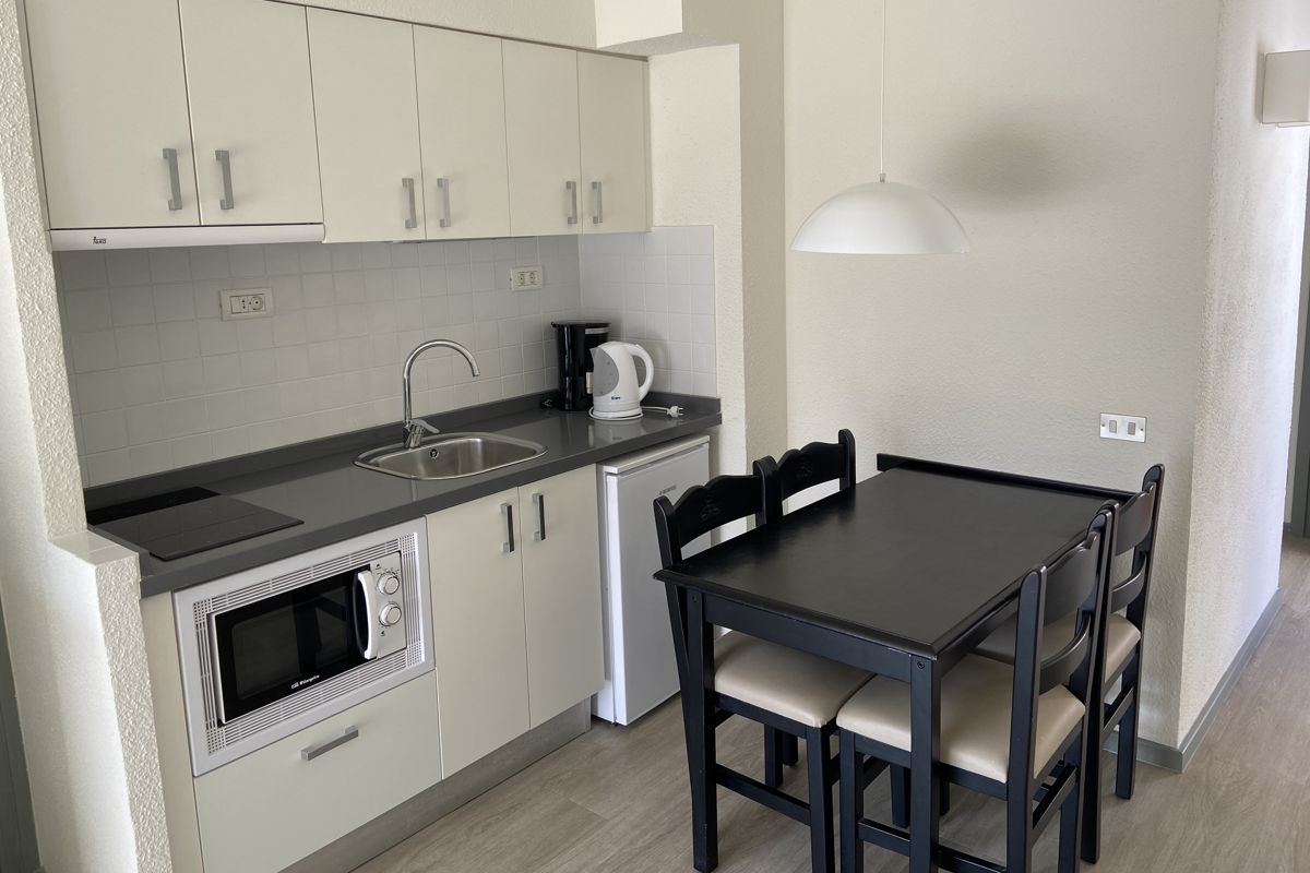 Small kitchen with stove, sink, microwave, fridge, and dining table for four in Tenerife.