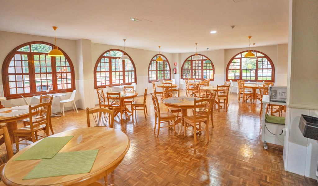 Dining area in Tenerife with round wooden tables and large arched windows.