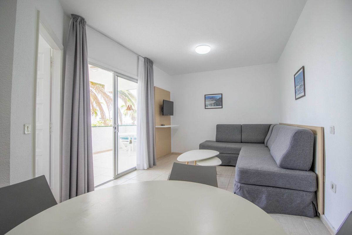 Living room with gray sofa, round table, wall TV and balcony view in Tenerife.