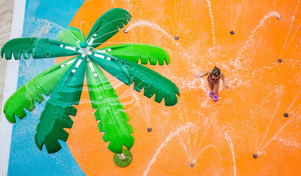 Child playing under a green water spray palm in Tenerife water park.