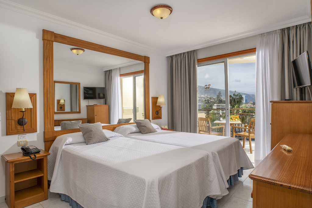 Hotel room with twin beds, wooden furniture, and balcony view in Tenerife.
