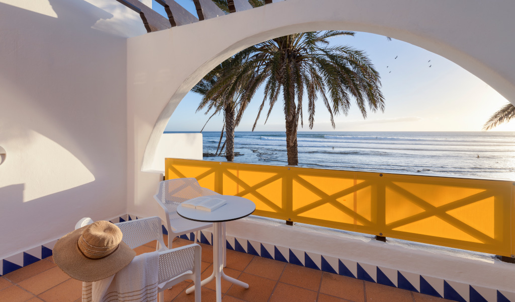 Terrace with table, chair, hat, and view of palm tree and ocean in Tenerife.