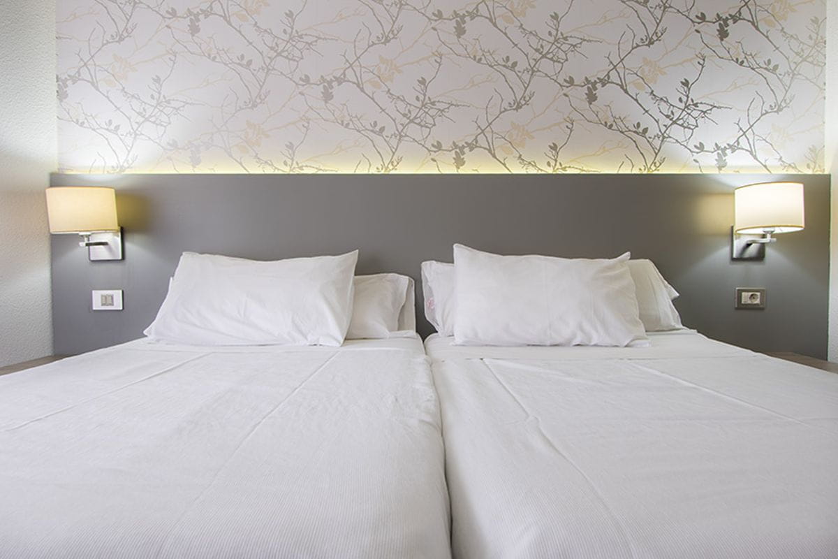 Two twin beds in a hotel room in Tenerife, with floral wallpaper and bedside lamps.