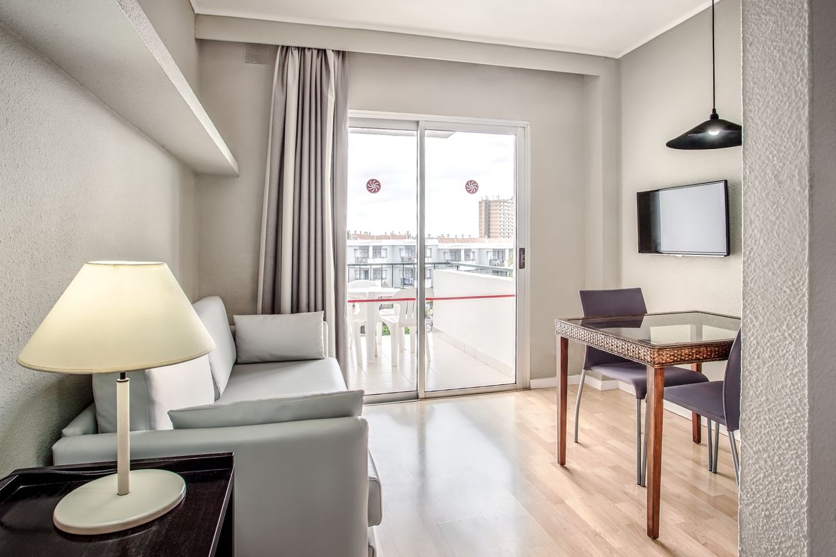 Living room with sofa, lamp, table, chairs, and a balcony view in Tenerife.