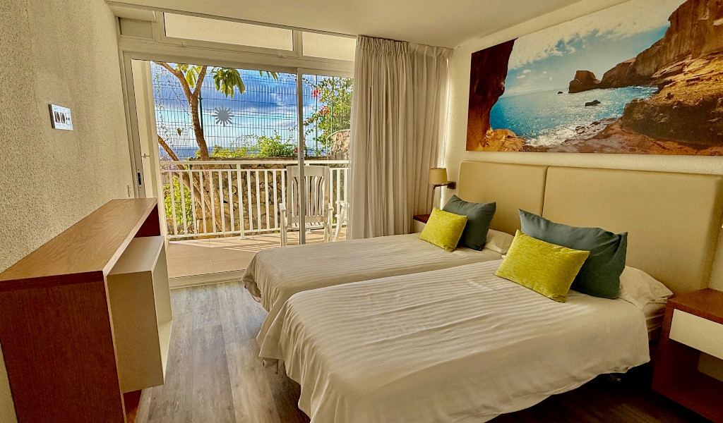 Twin beds in a hotel room with a view of Tenerife balcony and sea painting.