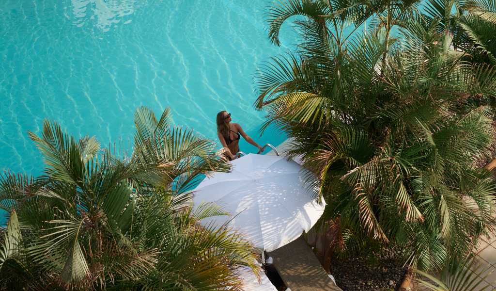 Woman relaxing by a pool with palm trees and a white parasol in Tenerife.