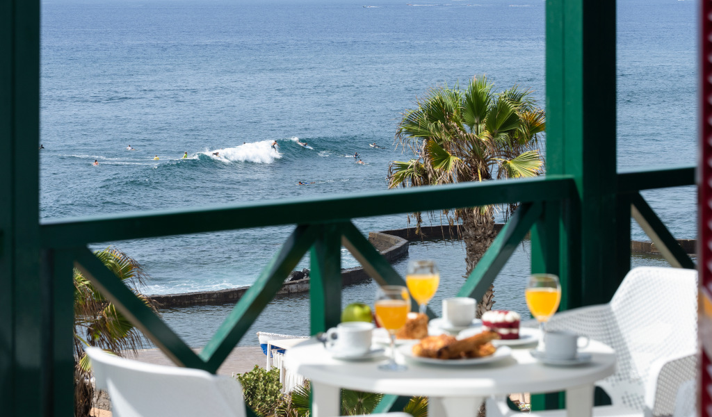Balcony with breakfast overlooking ocean and surfers in Tenerife.