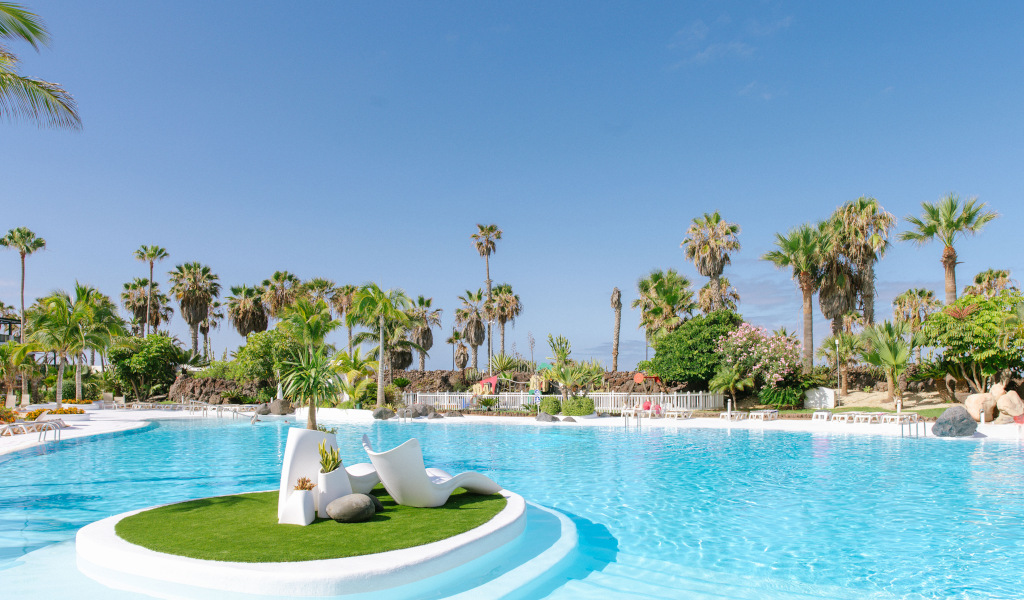 Swimming pool with palm trees and a sun lounger on a green island in Tenerife.