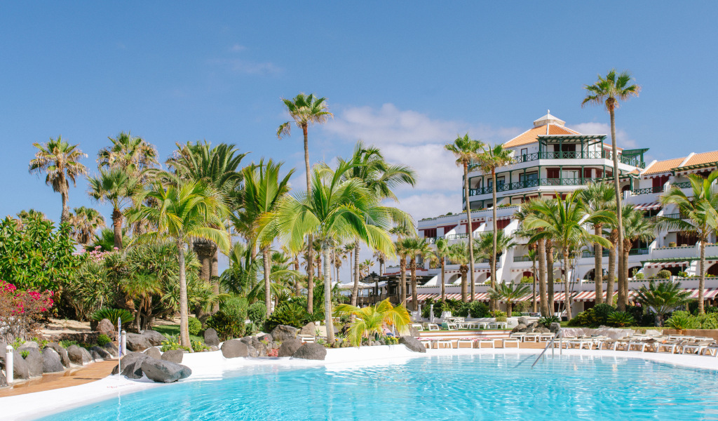 Tropical garden and pool at a hotel in Tenerife with palm trees and blue sky.