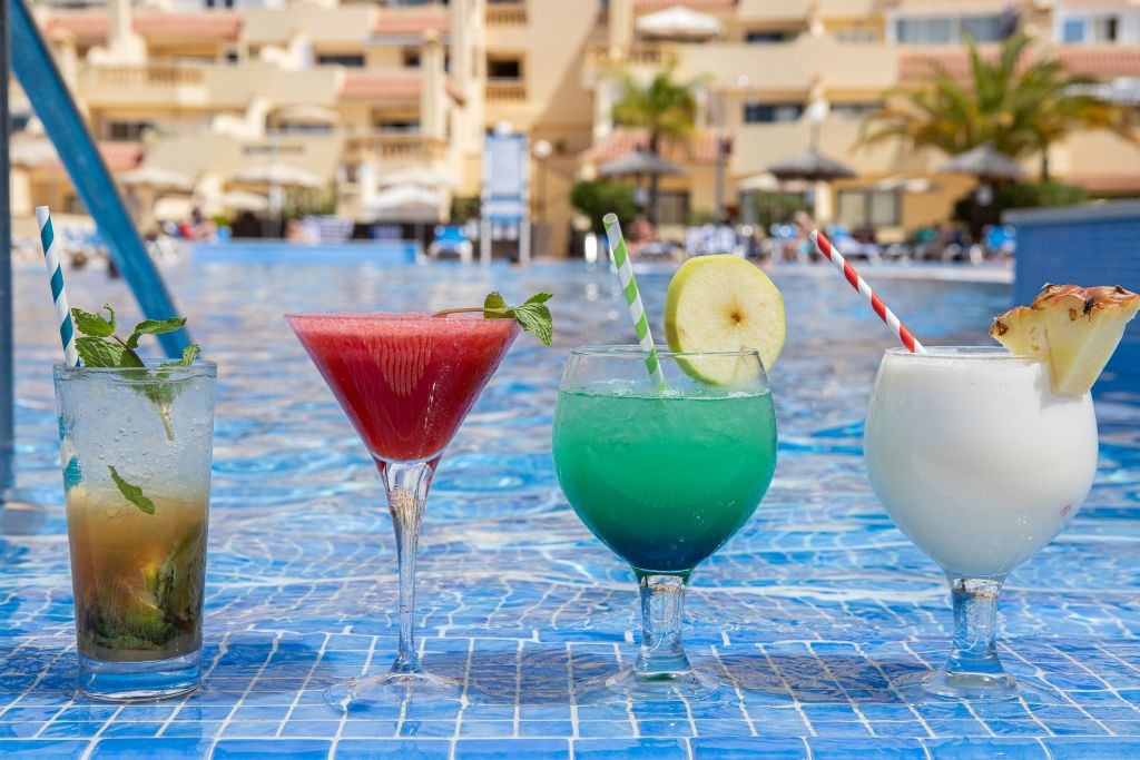 Four cocktails by a pool in Tenerife, each with a colorful straw and garnish.
