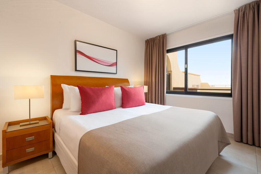 Modern bedroom with double bed, red pillows, and window view in Tenerife hotel.