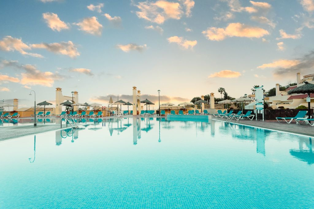 Outdoor swimming pool with sun loungers and umbrellas in Tenerife resort at sunset.