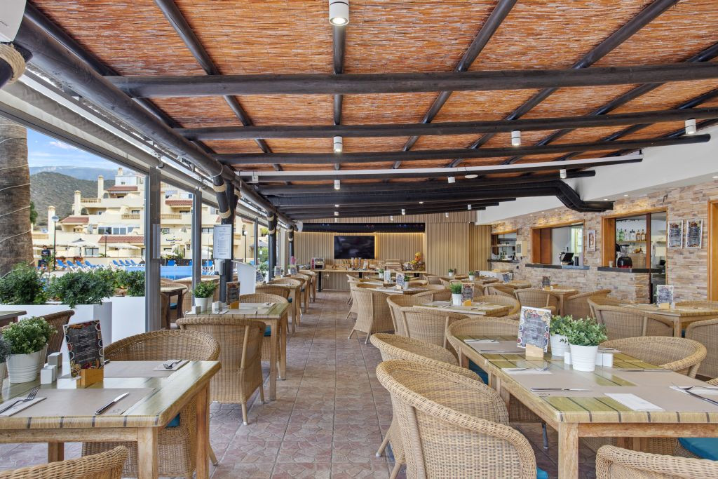 Outdoor dining area with wicker chairs and wooden tables in Tenerife restaurant.